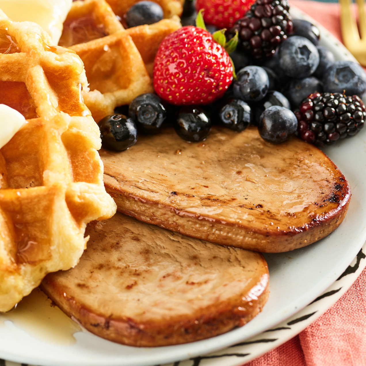 Plate with waffles Meati maple breakfast patty and a variety of berries on a white plate.